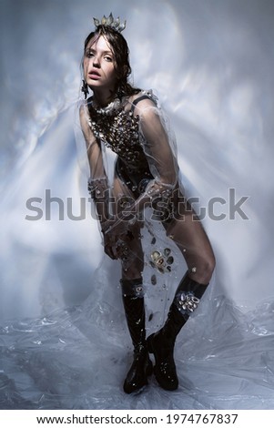 Woman in long transparent dress with seashells, black boots, crown of seashells. Creative illumination with glare on the wall