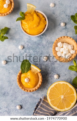 Mini tarts with lemon curd, mini meringue, lemon slices and mint on blue concrete background. Top view. Selective focus.