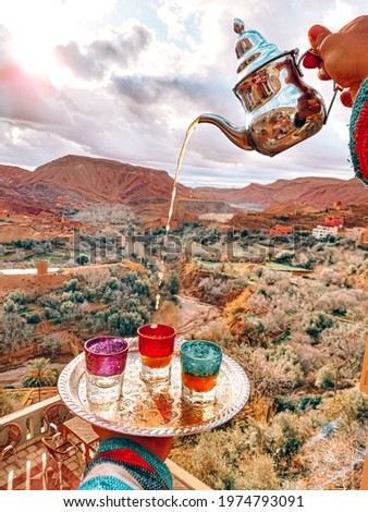 A hand pouring tea into a glass during Ramadan tea time in background of the Dades gorge in Morocco Royalty-Free Stock Photo #1974793091