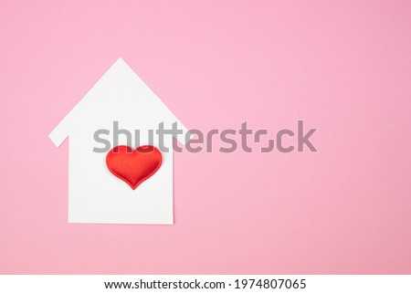 Small paper house with white and red hearts on a pink background. Copy space, top view.