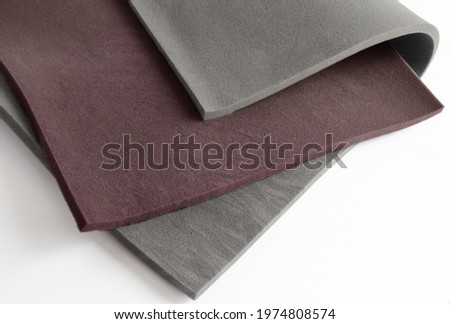 curved folds of two gray and brown spongy foam sheets on a white background. absorbent foam material that is supple, elastic, textured.