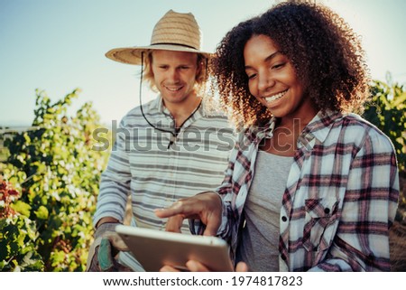 Diverse farmer couple working together on project standing in vineyards researching information on digital tablet 