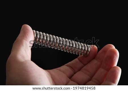 The male hand squeezes a metal spring on a black background.  