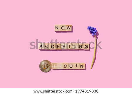 Now accepting Bitcoin sign with wooden blocks on pink background, crypto coin and spring flower. Banner for online retailers about paying with cryptocurrency