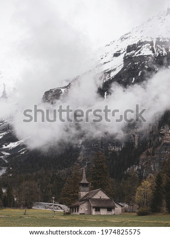 Old alpine church in the village of Kandersteg in Switzerland set against a misty mountain glacier background high in the alps.