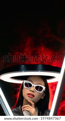 Cyberpunk face. Fashion banner. Sci-Fi future. Red neon light art portrait of curious Asian girl in glasses with white halo in color smoke isolated on black copy space background.