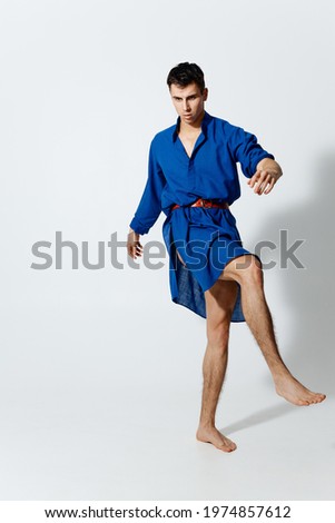 a man in a blue dress with a red belt on a light background dancing 