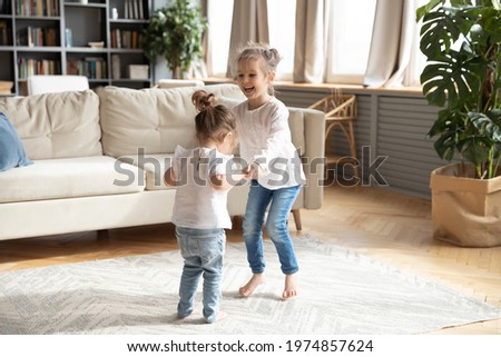 Overjoyed two small preschooler girls children have fun dancing together in cozy living room holding hands. Smiling little sisters kids jump listen to music play at home on weekend. Family concept. Royalty-Free Stock Photo #1974857624