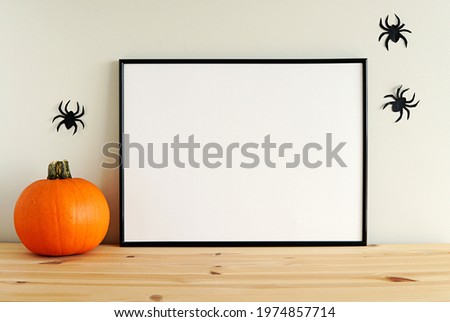 Black horizontal Halloween frame mockup for design presentation, pumpkin, paper spiders decorations, wooden shelf.