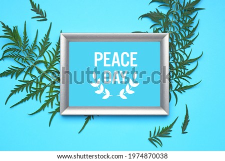 Frame with text PEACE DAY and green leaves on color background