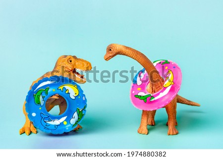 Toy dinosaur Tyrannosaurus with  holding colorful swimming circle in its paws on green background Holiday card Hello summer creative minimal concept 