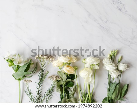 Various white flowers border on marble background. Ranunculus, eustoma, roses, alstroemeria frame. Flat lay, top view. Copy space