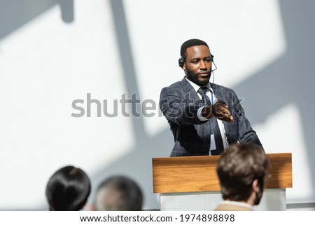 african american lecturer in headset pointing with hand near audience on blurred foreground