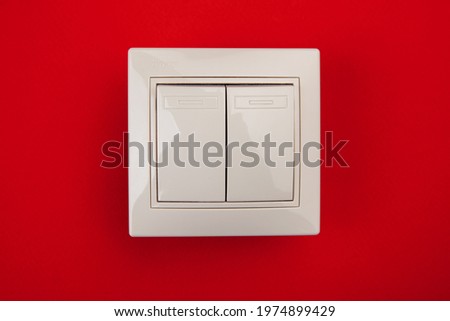 A square shaped white plastic light switch isolated on red