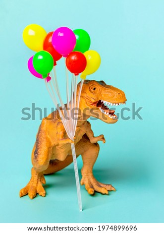 Toy dinosaur Tyrannosaurus with  holding colorful air balloons in its paws on blue background