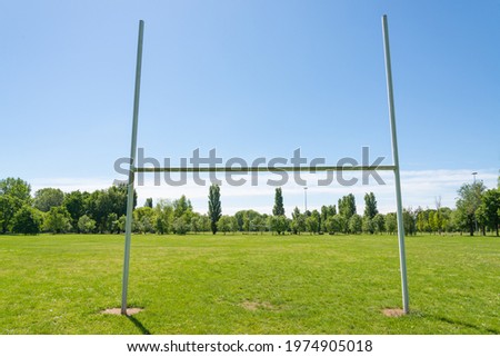 Isolated rugby goal post in a pitch of a park in Milan, Italy. Green field and green trees. Blue sky on the background.