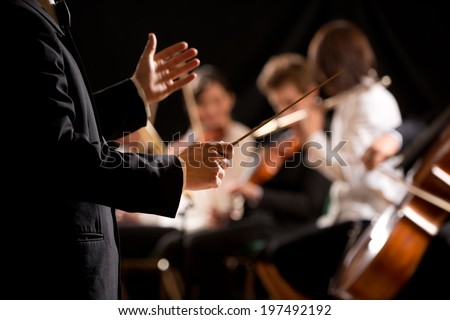 Conductor directing symphony orchestra with performers on background, hands close-up. Royalty-Free Stock Photo #197492192