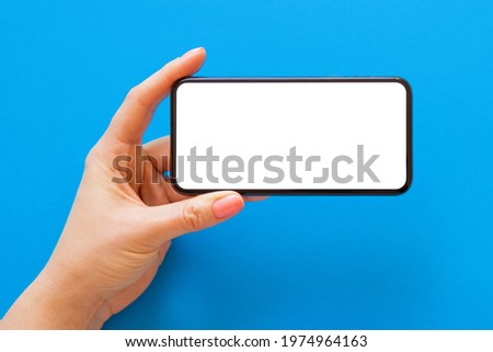 Mobile phone with empty white screen held in hand horizontally on blue background