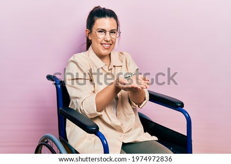 Young hispanic woman sitting on wheelchair smiling with hands palms together receiving or giving gesture. hold and protection 