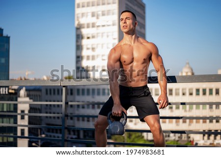 Powerful sport man lifting up a heavy kettle ball in a gym, body building exercise. Body building workout in an outdoor gym.