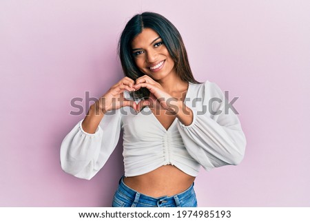 Young latin transsexual transgender woman wearing casual clothes smiling in love doing heart symbol shape with hands. romantic concept. 