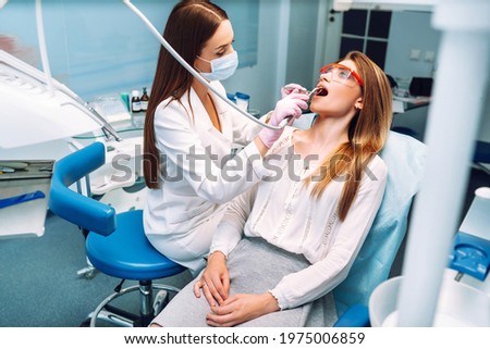 Young woman opening her mouth wide during treating her teeth by the dentist. Hands of a doctor holding dental instruments near patient's mouth. Healthy teeth and medicine concept. Royalty-Free Stock Photo #1975006859