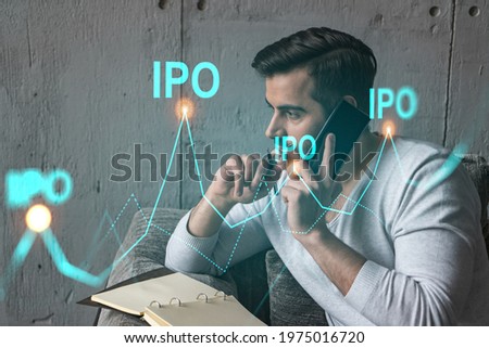 Handsome analyst in casual long sleeve talking phone, taking notes at office workplace try to analyze IPO project. Double exposure. Initial public offering hologram. Royalty-Free Stock Photo #1975016720