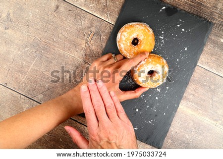 Conceptual image of a mans hand over a womans hand suggesting she exercises restraint in picking up the ring doughnut Royalty-Free Stock Photo #1975033724