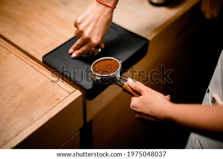 view of baristas hand tamping coffee in portafilter before making fresh drink in coffee machine at coffee shop. Royalty-Free Stock Photo #1975048037