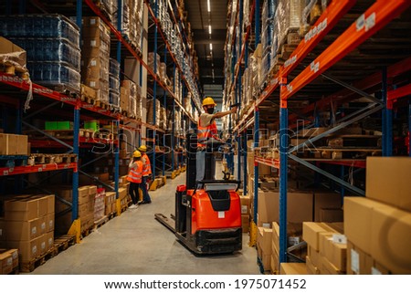 Male worker with face mask scanning bar-code on package boxes while driving forklift Royalty-Free Stock Photo #1975071452