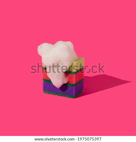 Yellow, red and purple sponges with white foam soap on magenta background. Minimal kitchen concept of dishwashing. Creative colorful composition.