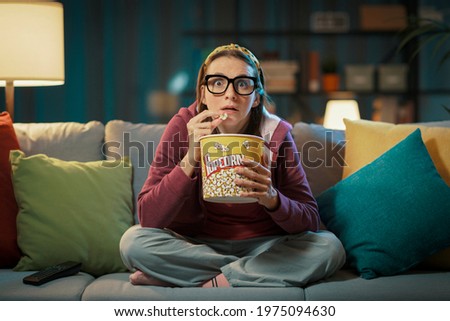 Woman watching a suspense movie and eating popcorn Royalty-Free Stock Photo #1975094630