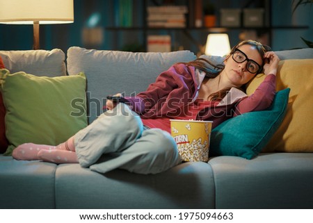 Woman lying down on the sofa at home and watching TV Royalty-Free Stock Photo #1975094663
