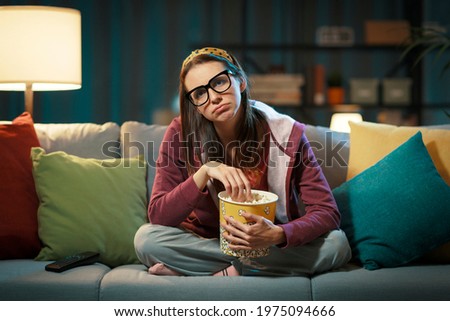 Woman watching a boring movie on TV and eating popcorn