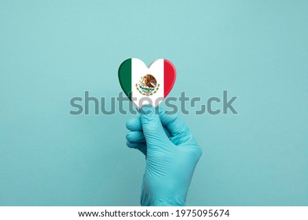 Hands wearing protective surgical gloves holding Mexico flag heart