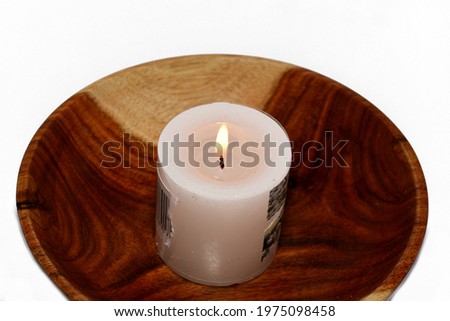 a burning candle in a brown wooden bowl isolated on a white background, a closeup of a white wax candlelight flame