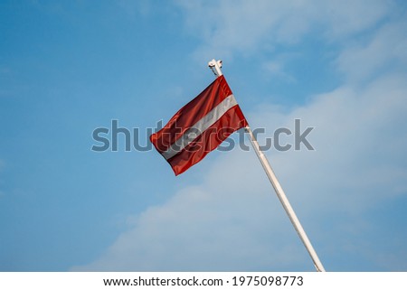 Latvian red and white striped flag against blue sky (815)