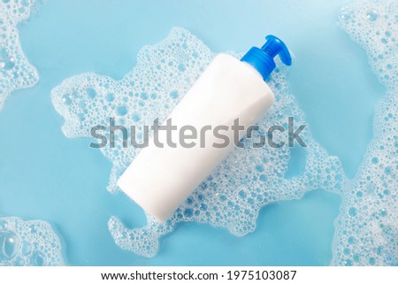 white free shampoo bottle in the water with soap bubbles, 
lather and water droplets. Top view on blue background Royalty-Free Stock Photo #1975103087