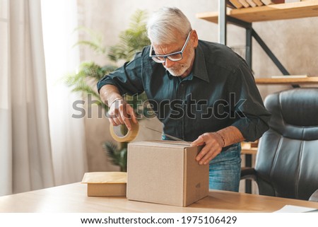 Seal the parcel. A grown man sends a box of goods by mail. Return of purchase to the online store. Royalty-Free Stock Photo #1975106429