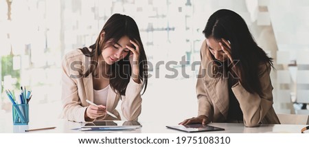 Two businesswoman holding their heads and feeling stressed and confused about their work. Royalty-Free Stock Photo #1975108310