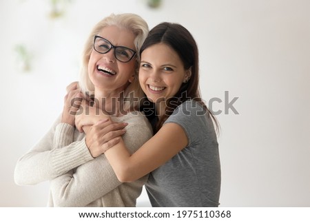 Family portrait of happy mature old mother and adult teenage daughter hug and cuddle spend weekend time together. Smiling middle-aged 60s mom and grownup teen child embrace show love and care. Royalty-Free Stock Photo #1975110368