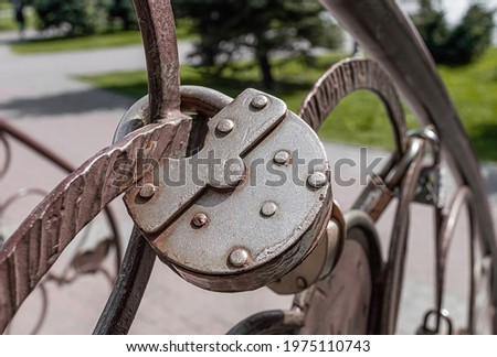 Old weathered padlock hanging on decorative metal fence.