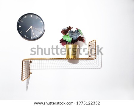 gold vase of flowers on a gold shelf with black clock on a white wall, interior design Royalty-Free Stock Photo #1975122332