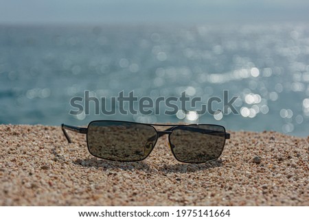 Dark sunglasses on the sand against the sea. blurred background with bokeh elements. Stock Photo