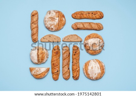 Food knolling with homemade sourdough bread. Round loaves and baguettes made with sourdough arranged symmetrically on a blue background. Royalty-Free Stock Photo #1975142801