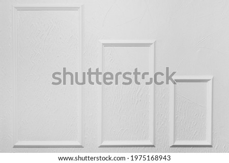 Three white frames of different sizes on a white wall