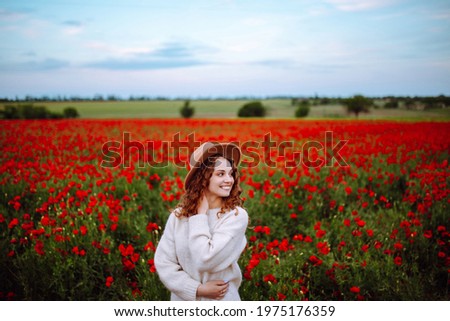 Girl in a beautiful colorful poppy field. Young woman posing in the garden with lovely red flowers. Bright colors. Girl in a hat with long beautiful hair