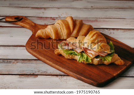 Fresh croissant with ham and lettuce leaves on a light wooden background	