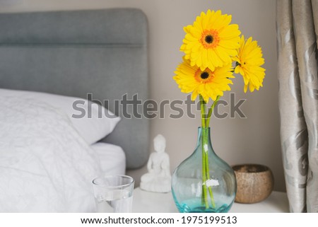 Good morning concept. Sunny yellow gerbera flowers and glass of water on the bedside table. Simple details for good mood for all day. Bedroom Design Ideas. Selective focus, copy space.
