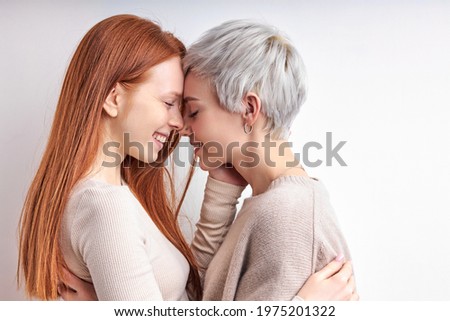 Side View Portrait Of Pretty Redhead Woman And Short Haired Lady Hugging, Feeling Love, Standing Closely To Each Other, Enjoying Time Together, Smiling Happily. LGBT, Lesbians, lgbt couple Royalty-Free Stock Photo #1975201322
